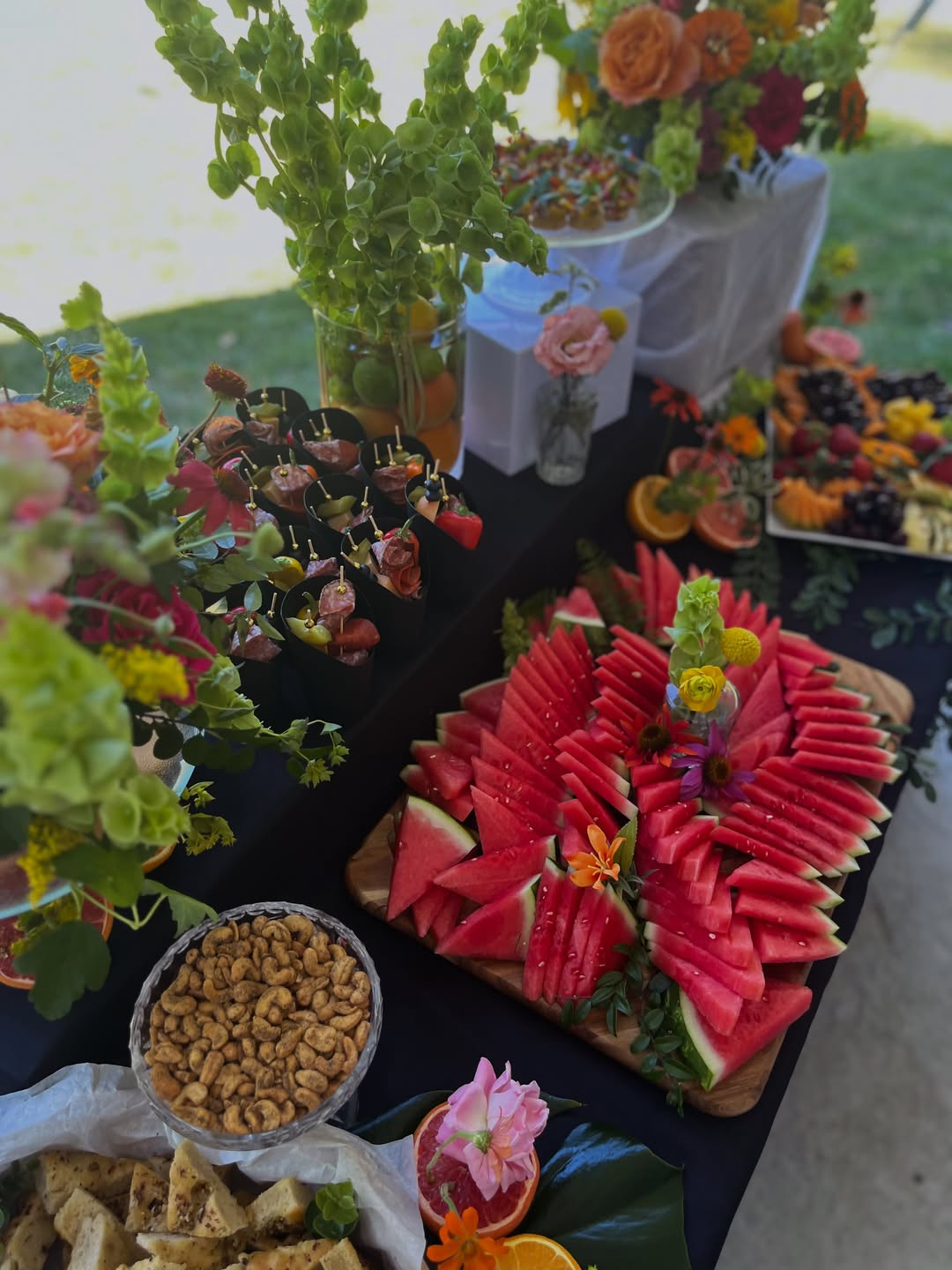 Grazing table with sliced watermelon, fresh fruit, nuts and edible flowers